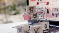 A small shopping cart with packages on a laptop keyboard in front of an online store.
