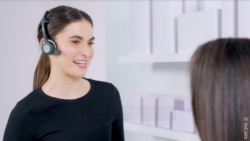 A woman is wearing a headset while standing in front of a shelf with another person; copyright: VoCoVo