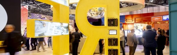 Large yellow stand installation with giant letters spelling out “RE-USE,” surrounded by trade fair visitors under a modern hall ceiling; copyright: Messe Düsseldorf/A. Wiese
