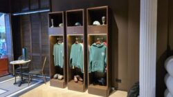 Salesroom made of dark wood with three open wooden lockers displaying sweatshirts, caps, and shoes, next to a small table with chairs; copyright: beta-web/Pott 