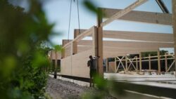 Construction site of a supermarket built using timber frame construction with exposed wooden beams and a construction worker in the foreground; Copyright: Aldi Nord