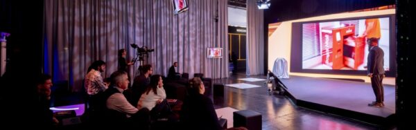 “Retail Uncovered” presentation stage with modern design and screen showing a product demo while visitors sit in front of the stage and watch; copyright: Messe Düsseldorf/A. Wiese