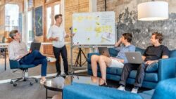 Four people sit together and discuss their business plans on a whiteboard; Copyright: Austin Distel / Unsplash