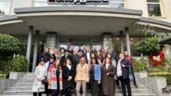A group of business-minded people is standing on a staircase in front of a building entrance with the company sign 'Shopguard 