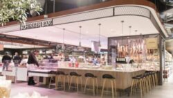 Modern ham bar in a grocery store with counter, bar stools, hanging ham legs, and employees preparing meat products; copyright: Zurheide 