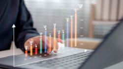 A person works on a laptop while a bar and line chart shows rising prices for shopping baskets over the months. 
