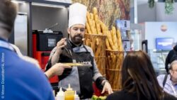 Person wearing a chef's hat at a food service equipment stand at EuroShop, surrounded by visitors 