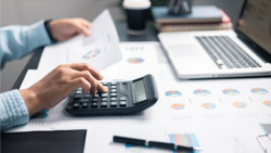 A person calculates with a calculator and analyzes financial documents at a desk; Copyright: Adobe Express